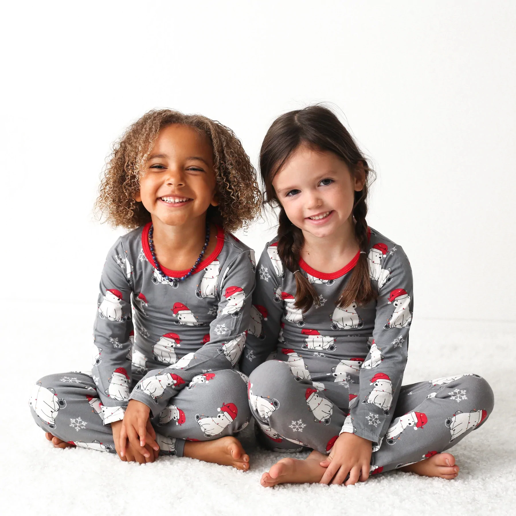 Two kids sitting on the floor and wearing festive pyjamas