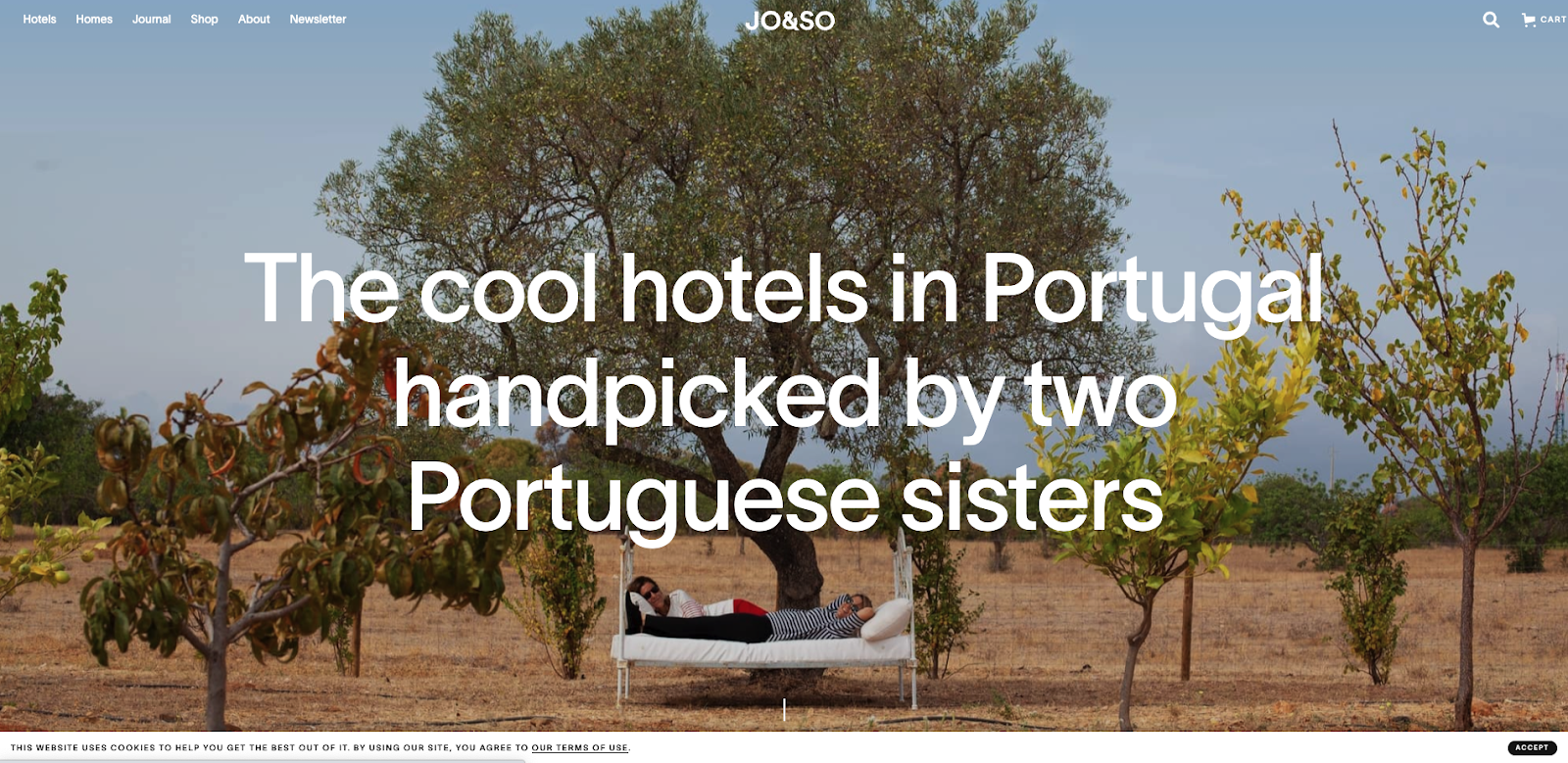 JO&SO のホームページのスクリーンショット。「ポルトガルの 2 人の姉妹によって厳選されたポルトガルのクールなホテル」という見出しが付いた、野原の木々と真ん中のベッドで寝ている 2 人の人物のページ全体の画像が特徴です。